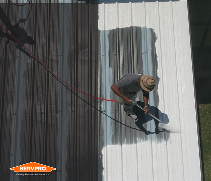 silicone roofing, aerial shot of a roof getting painted with seal, man working on top of it, SERVPRO logo in corner