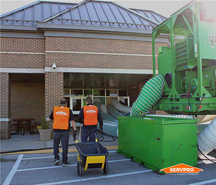 2 SERVPRO of Central St. Petersburg crew in orange vests walking into a school next to a big, green desiccant dehumidifier